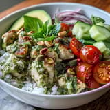 Vibrant Pesto Chicken Bowl with tender chicken, fluffy rice, fresh veggies, and toasted pine nuts on a plate.