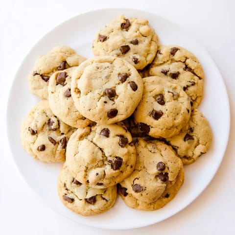 Golden-brown Chocolate Chip Cookies piled on a white plate, showcasing soft centers and rich chocolate chunks ready to be enjoyed.