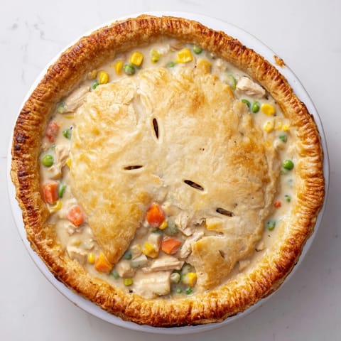 A warm slice of Chicken Pot Pie is served on a plate, revealing tender chicken, peas, and carrots in rich gravy.