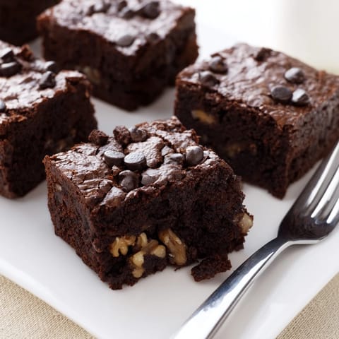 A close-up of rich chocolate brownies cut into squares, revealing a dense, chewy center with chopped walnuts.