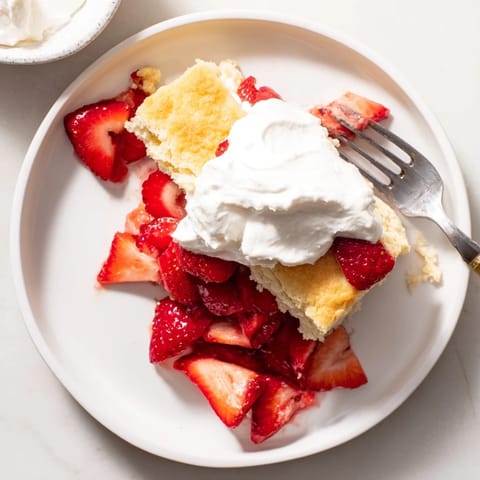 A close-up of classic American Strawberry Shortcake, featuring tender biscuits topped with glistening strawberries and soft clouds of fresh whipped cream.
