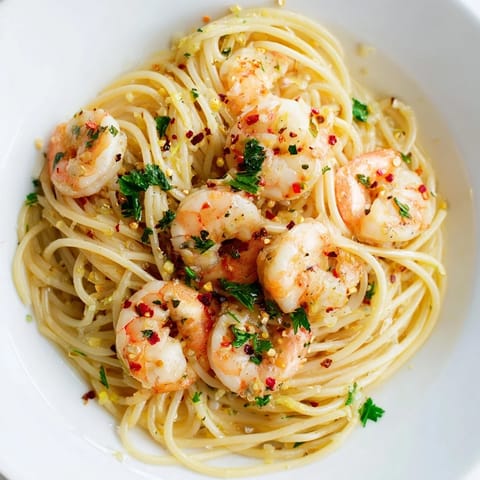 A close-up of juicy shrimp draped in glossy lemon garlic sauce over perfectly cooked spaghetti, with a sprinkle of Parmesan and a wedge of lemon beside the plate.
