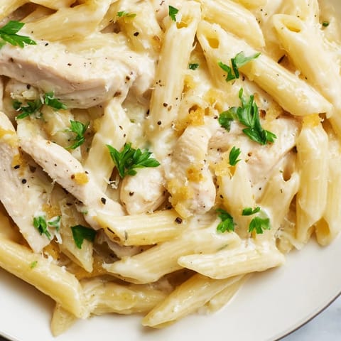 Golden-brown roasted chicken slices tossed with al dente penne, smothered in a creamy roasted garlic Parmesan sauce and garnished with fresh parsley.