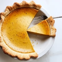 Freshly baked Pumpkin Pie with a golden, flaky crust and a silky spiced custard filling, served on a rustic wooden table.