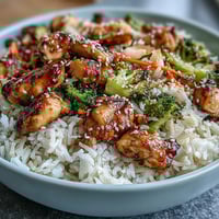 Hearty chicken and rice bowl with tender grilled chicken, colorful vegetables, and fluffy rice, garnished with fresh herbs and sesame seeds.  